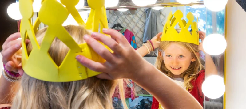 Tjej som testar prinsesskrona framför teaterspegel.