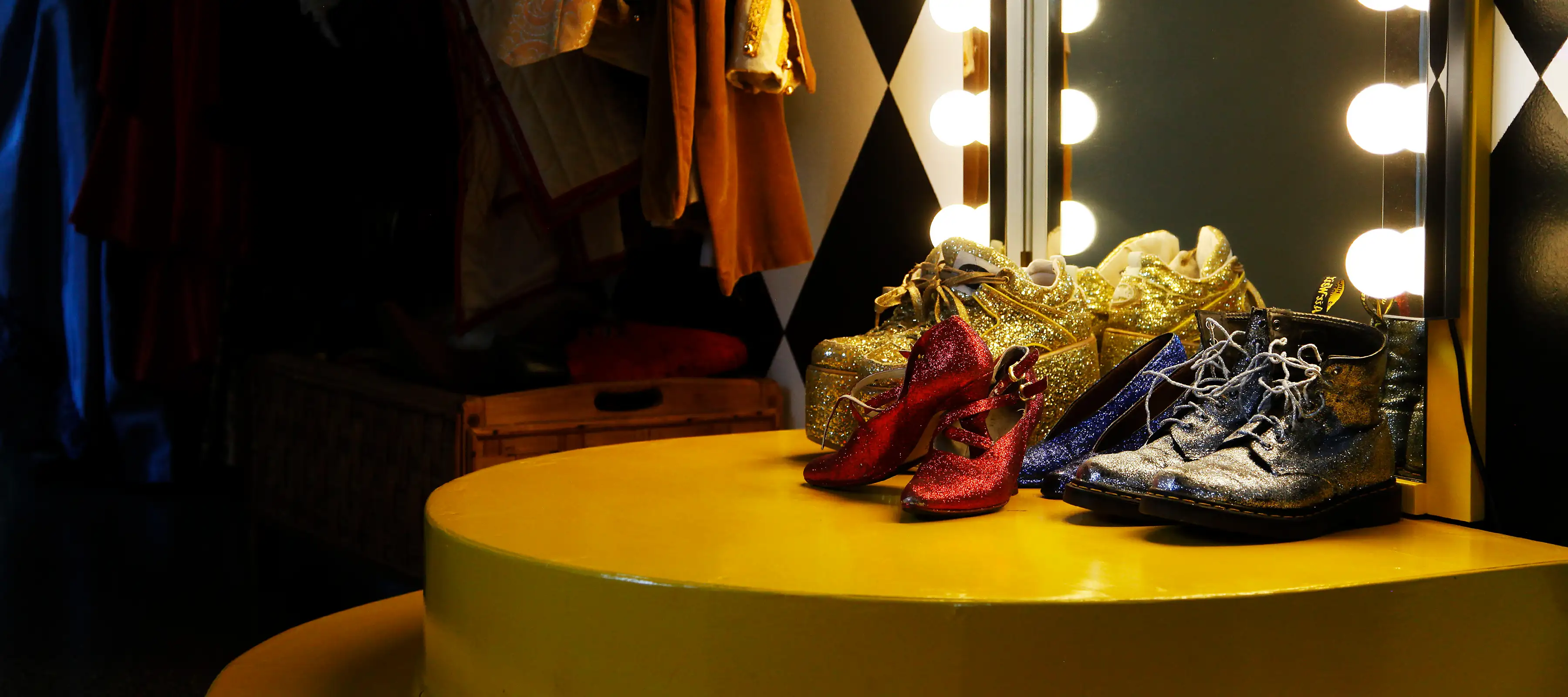 En teaterspegel med lampor och framför står gyllene skor.